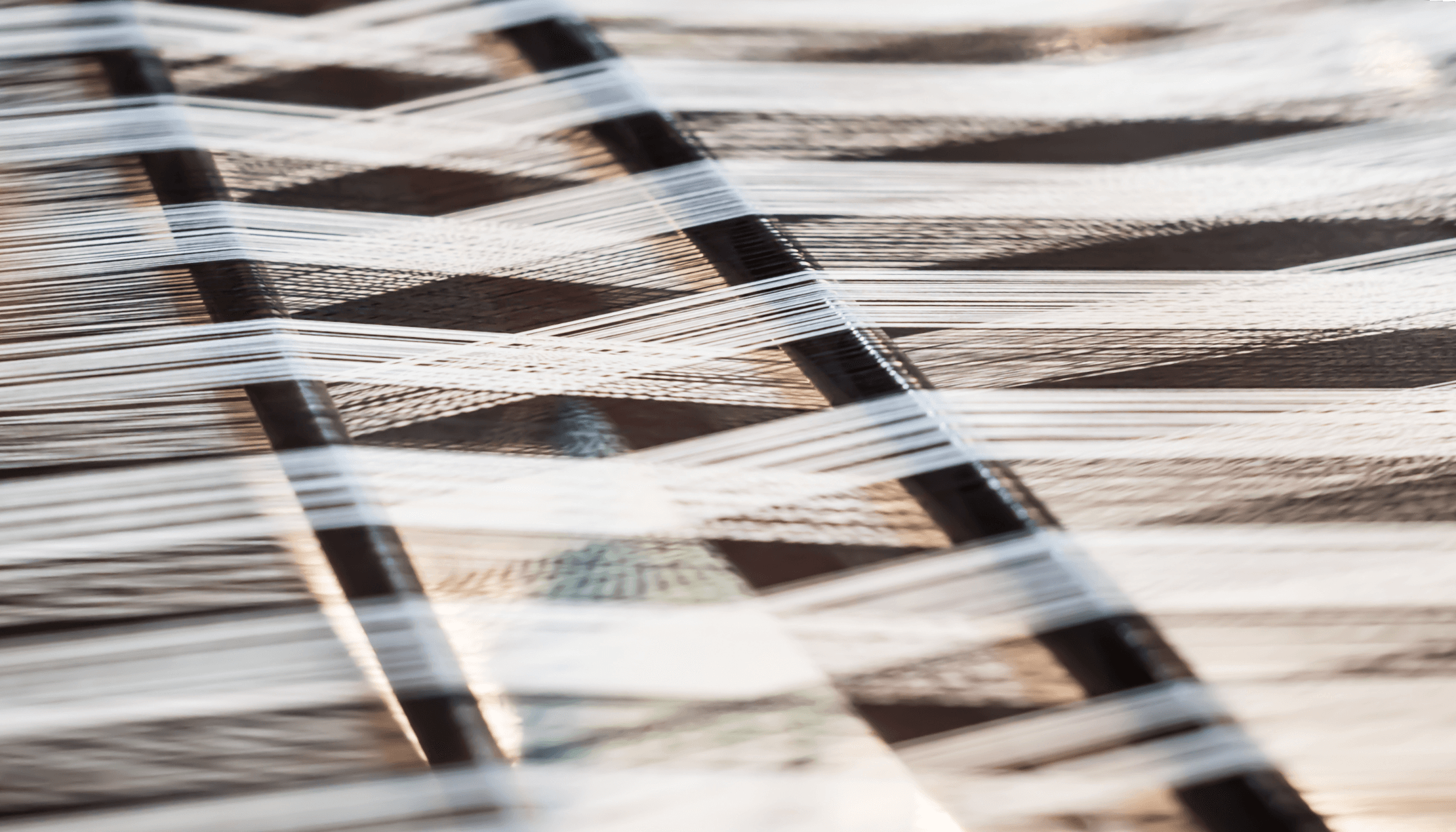 Close-up of interlaced threads on a loom held by wooden dowels